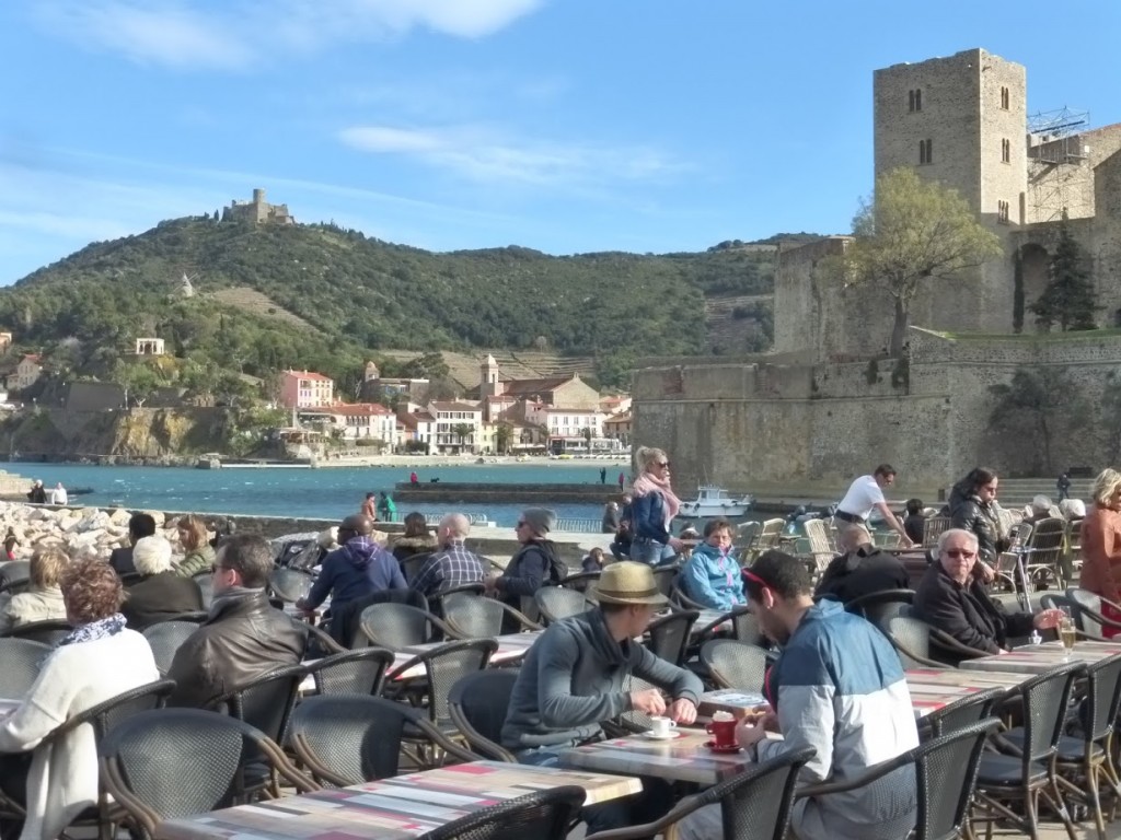 Turistas sentados em cafés a beira mar, com parte das montanhas que cercam Collioure