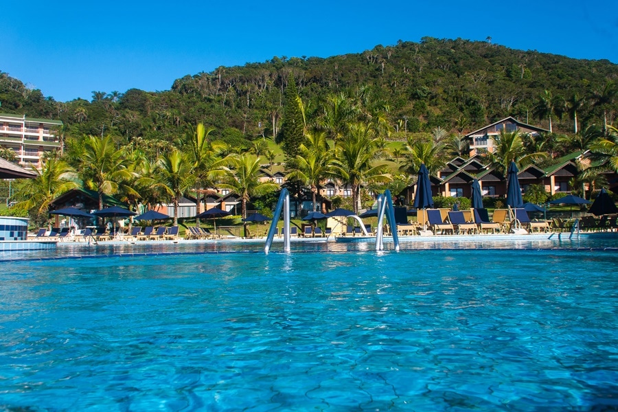 Piscina azul do resort com coqueiros e cadeiras de sol