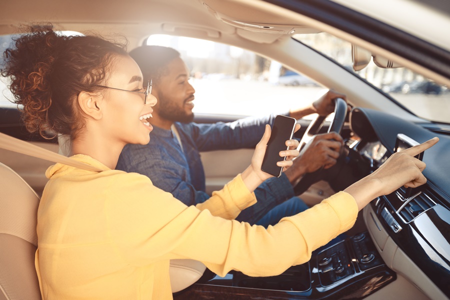 Mulher de blusa laranja dentro do carro ao lado de um homem com blusa azul